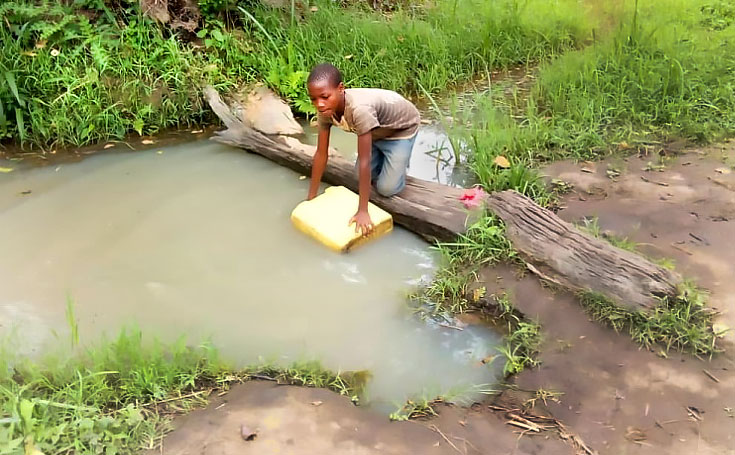 BEFORE: A young boy draws water from Kihanya's old water source.